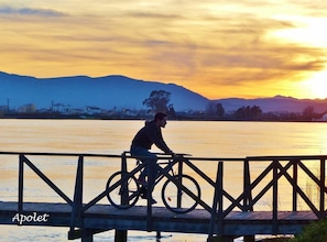 A person sitting on a bicycle on a wooden bridge over a body of water with mountains in the background. - Delta Hotel (Deltebre)
