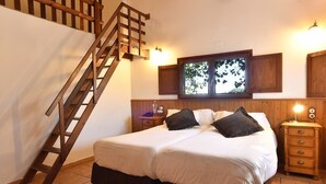 A bedroom with a wooden staircase, a bed with white bedding, a nightstand, and a window with a view of trees. - Delta Hotel (Deltebre)