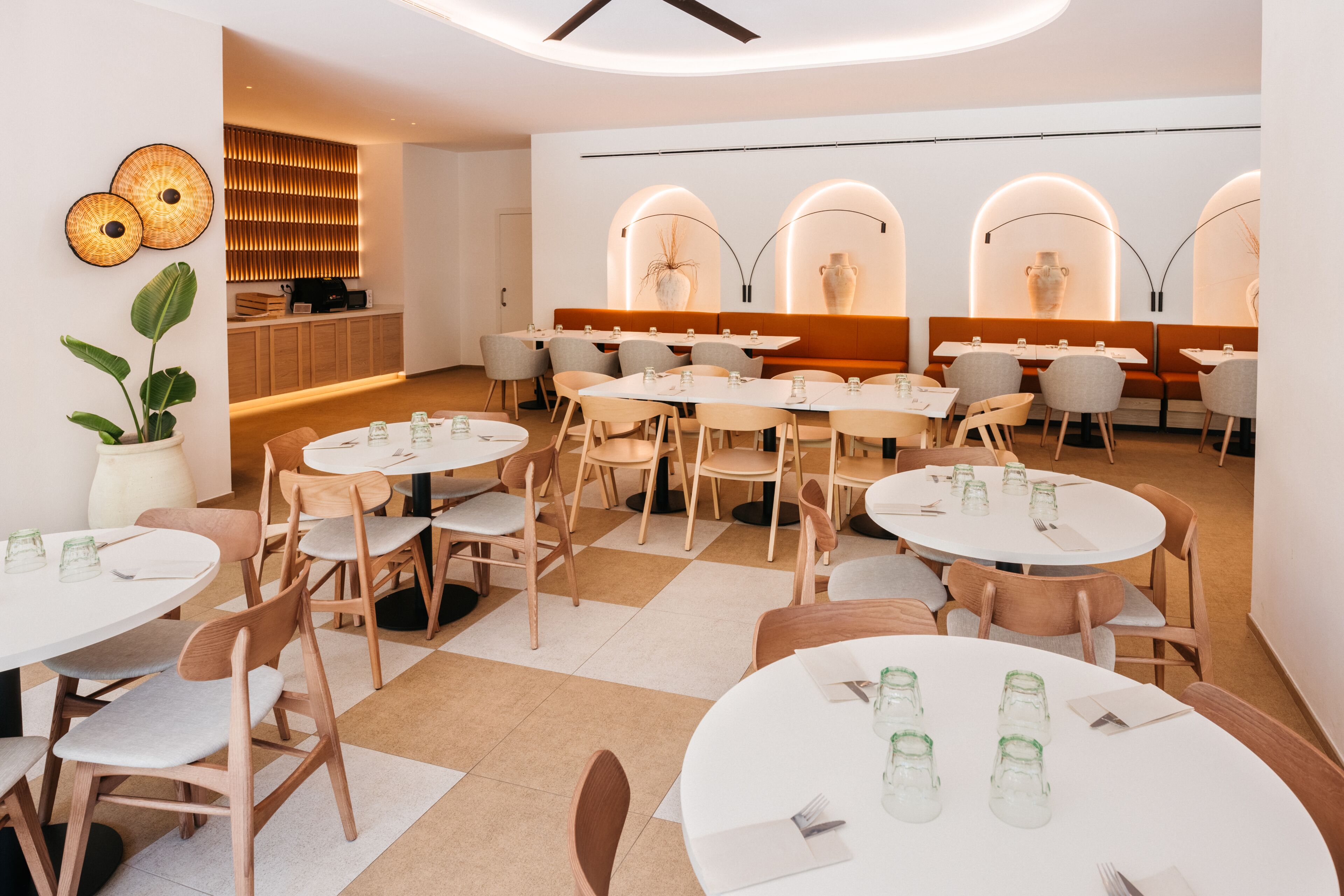 A modern dining area with round tables and chairs, a seating area with benches, and decorative wall elements.