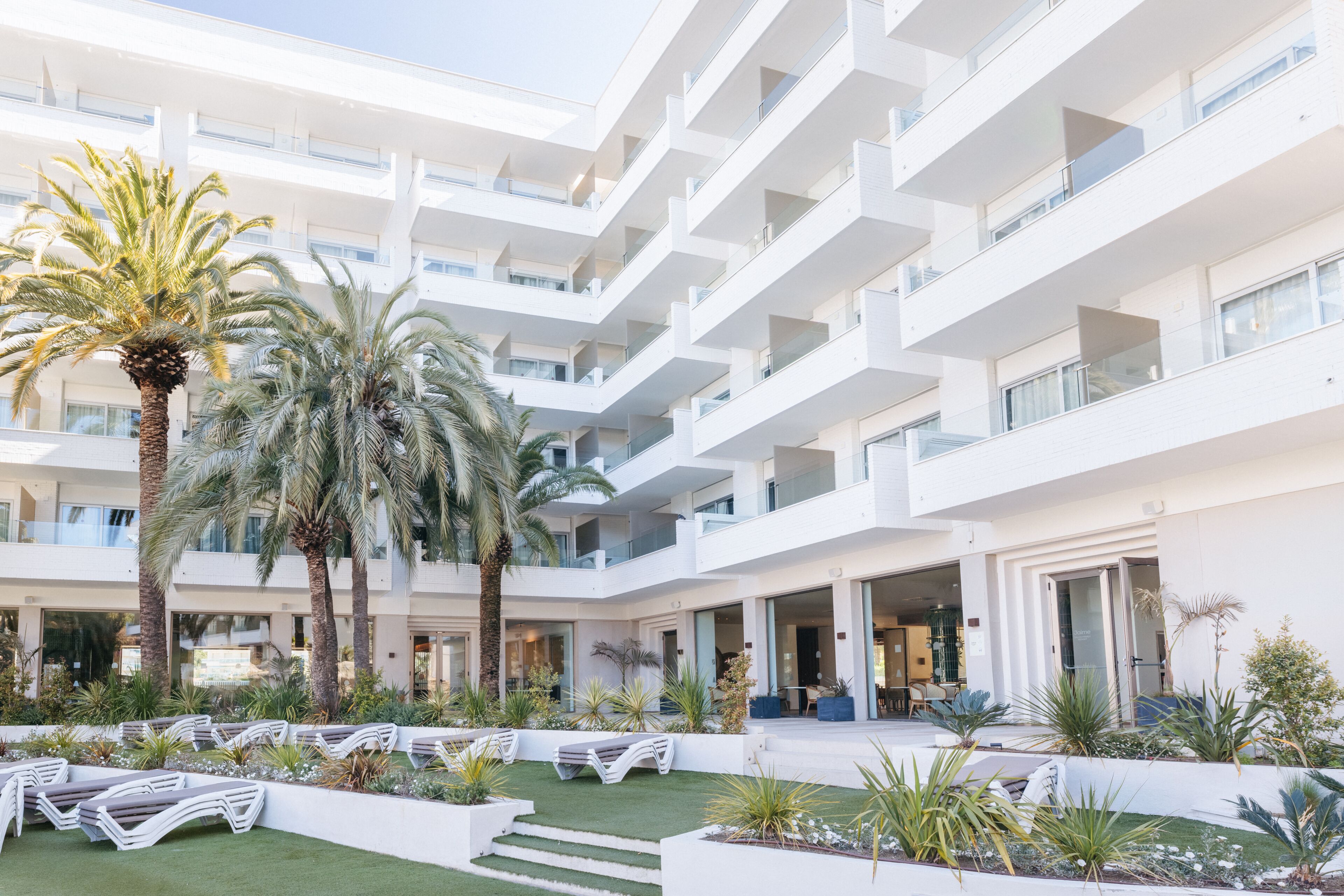 A multi-story hotel with balconies, a courtyard with palm trees, and outdoor seating.