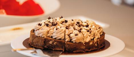 Una presentación de postres con un pastel de chocolate cubierto de crema batida y nueces, rodeado de otros dulces.