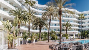 Un hotel de varios pisos con piscina, palmeras y mobiliario exterior.