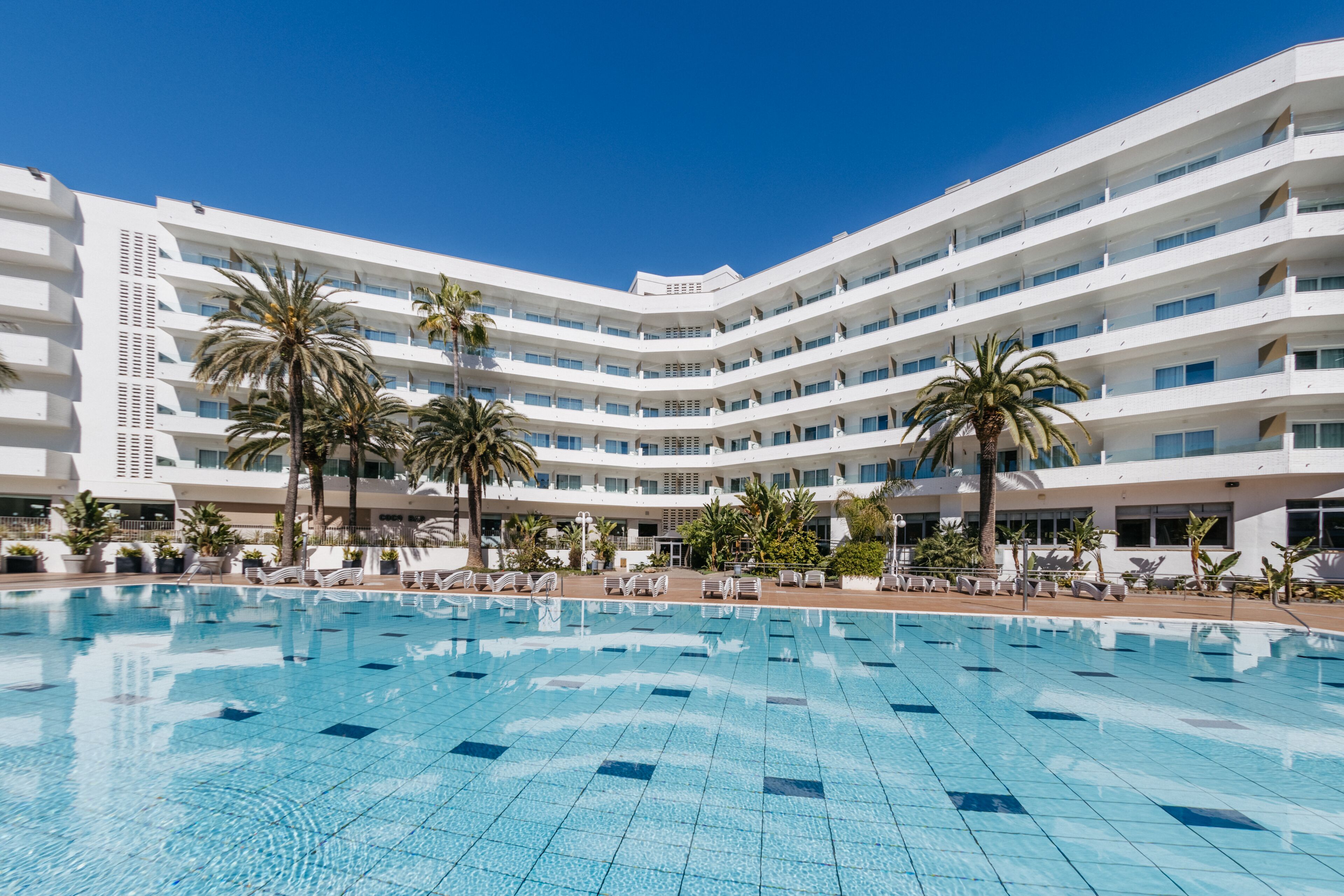 Um hotel com uma piscina grande, vários andares e palmeiras.