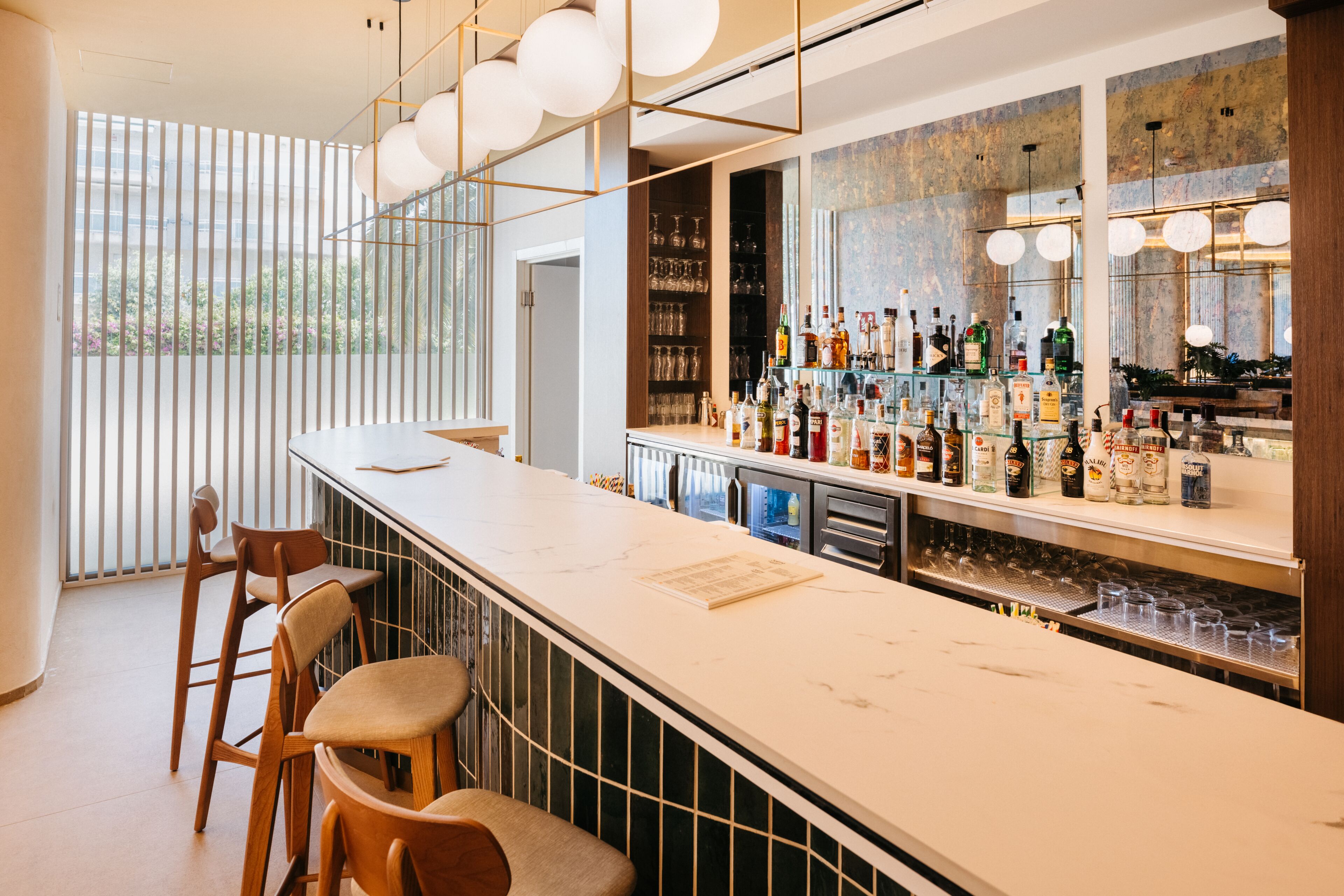 A modern bar area with a long counter, stools, and a variety of bottles and glasses.