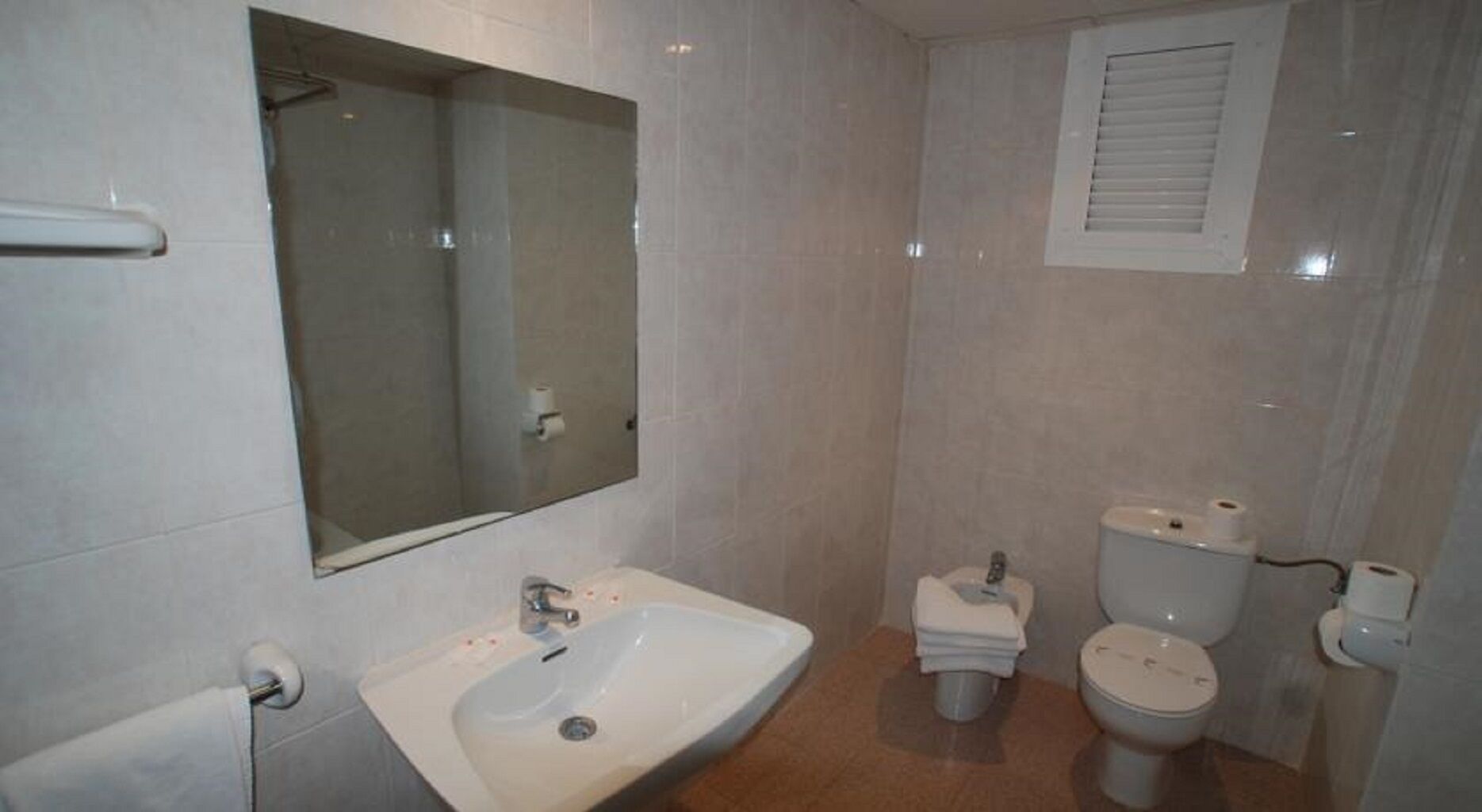 A bathroom with a sink, mirror, toilet, and a window.