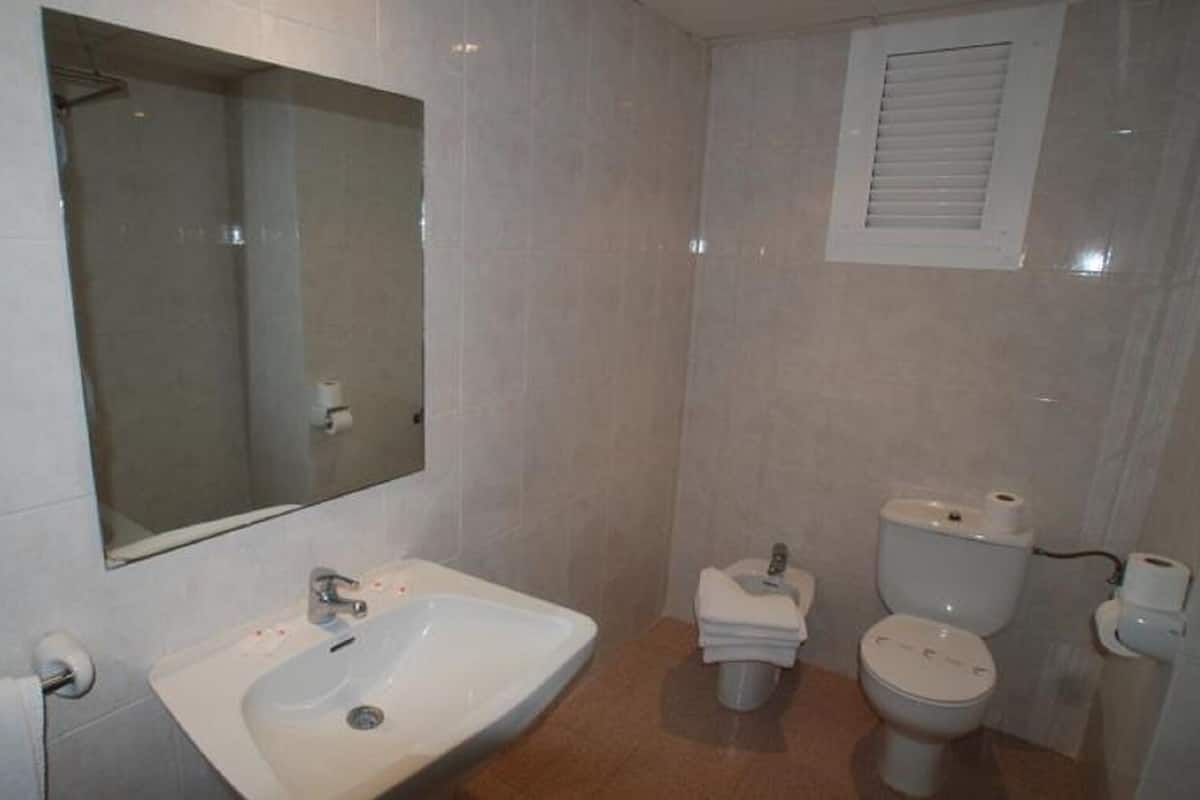 A bathroom with a sink, mirror, toilet, and a window.