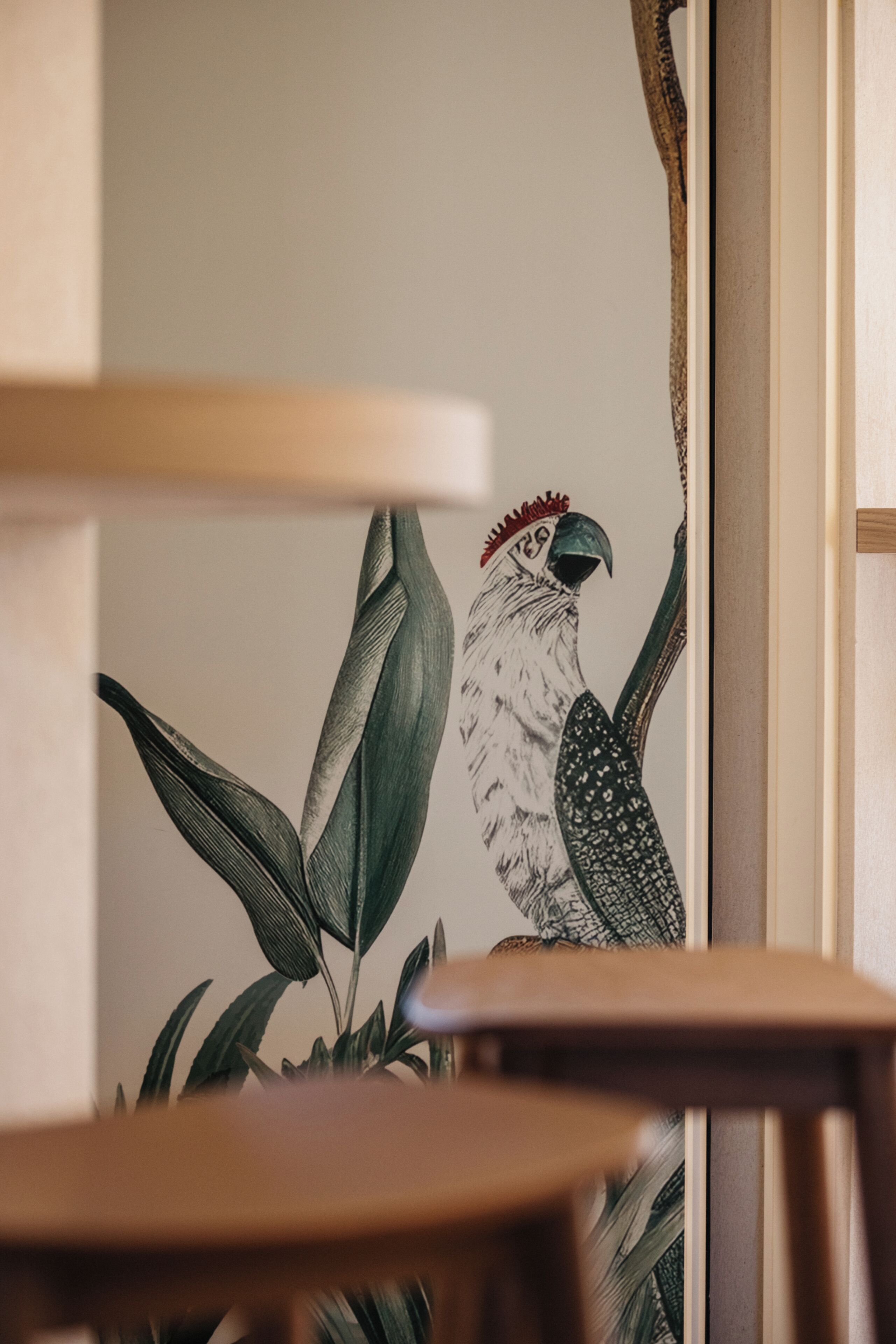 Pared con un mural de un ave y follaje, una silla de madera, y una vista parcial de un marco de puerta.