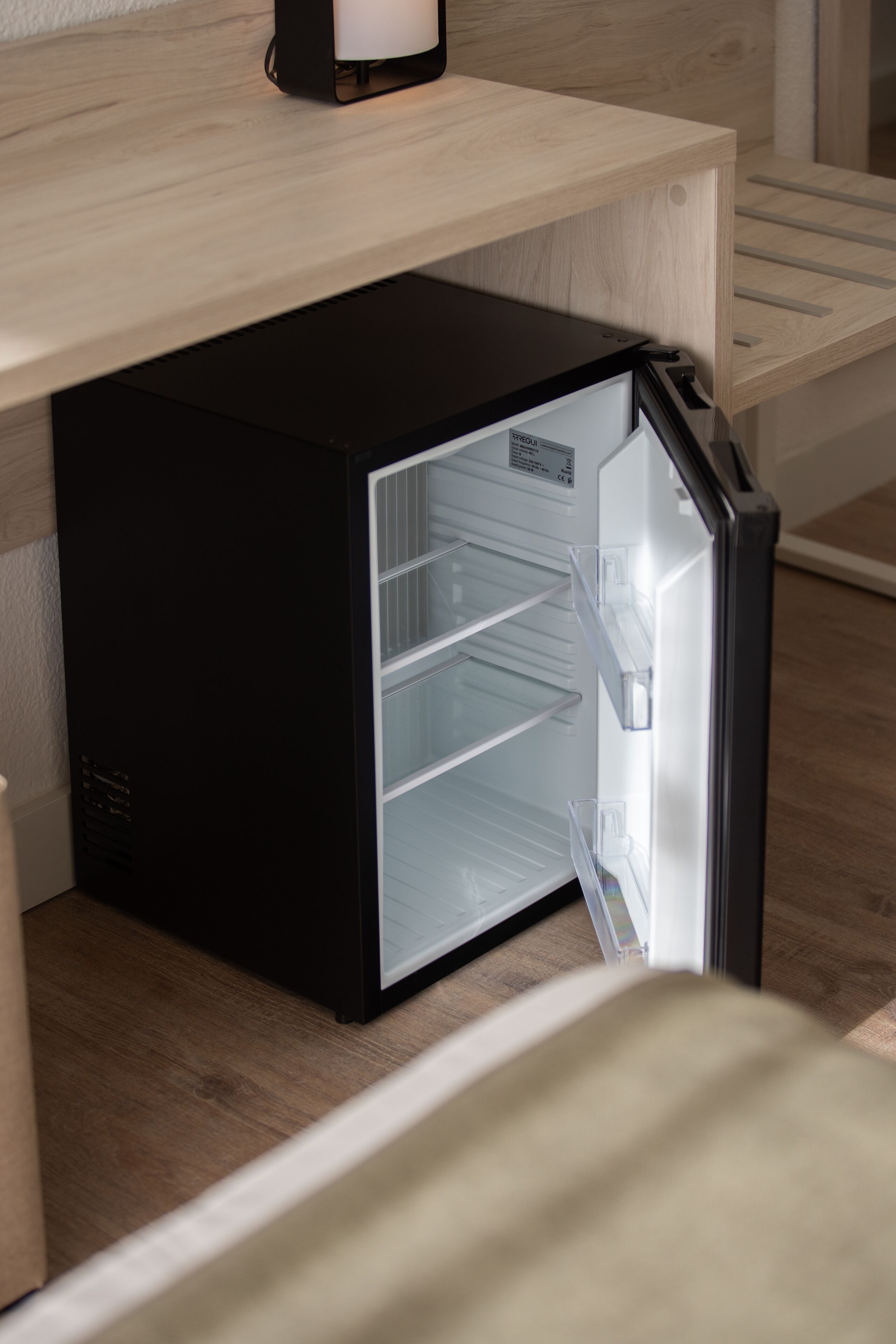 A compact black refrigerator with a transparent door, placed under a wooden counter.