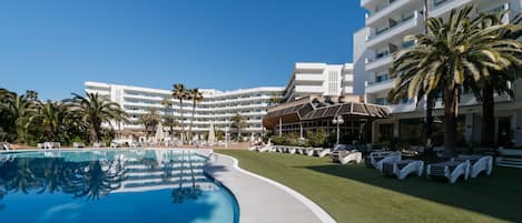 A swimming pool with lounge chairs, palm trees, and a hotel building in the background.