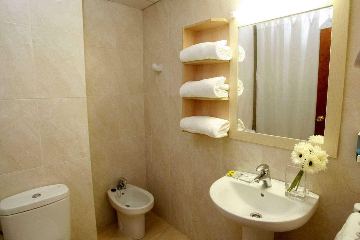 Une salle de bain comprenant des toilettes, un bidet, un lavabo et un miroir avec un porte-serviettes placé au-dessus.