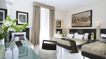 A hotel room with two beds, a glass table with a tablet, a vase with flowers, and framed pictures on the walls.