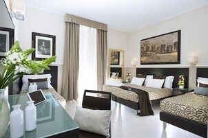 A hotel room with two beds, a glass table with a tablet, a vase with flowers, and framed pictures on the walls.