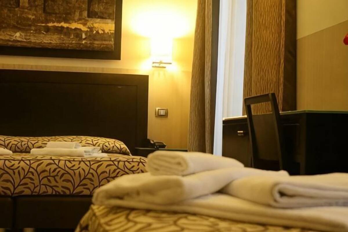 A hotel room with two beds, a desk, a chair, and a painting on the wall.