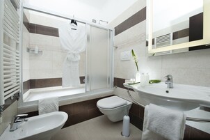 A modern bathroom with a glass shower enclosure, a bathtub, a toilet, and two sinks.