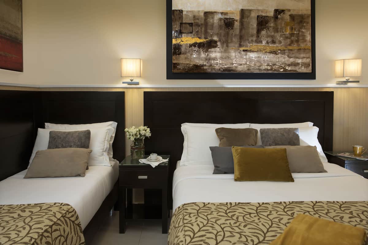 A hotel room with two beds, a nightstand, a lamp, and a large abstract painting on the wall.