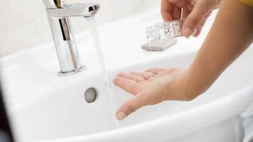 A hand under a running faucet with water flowing into a clear glass bottle.