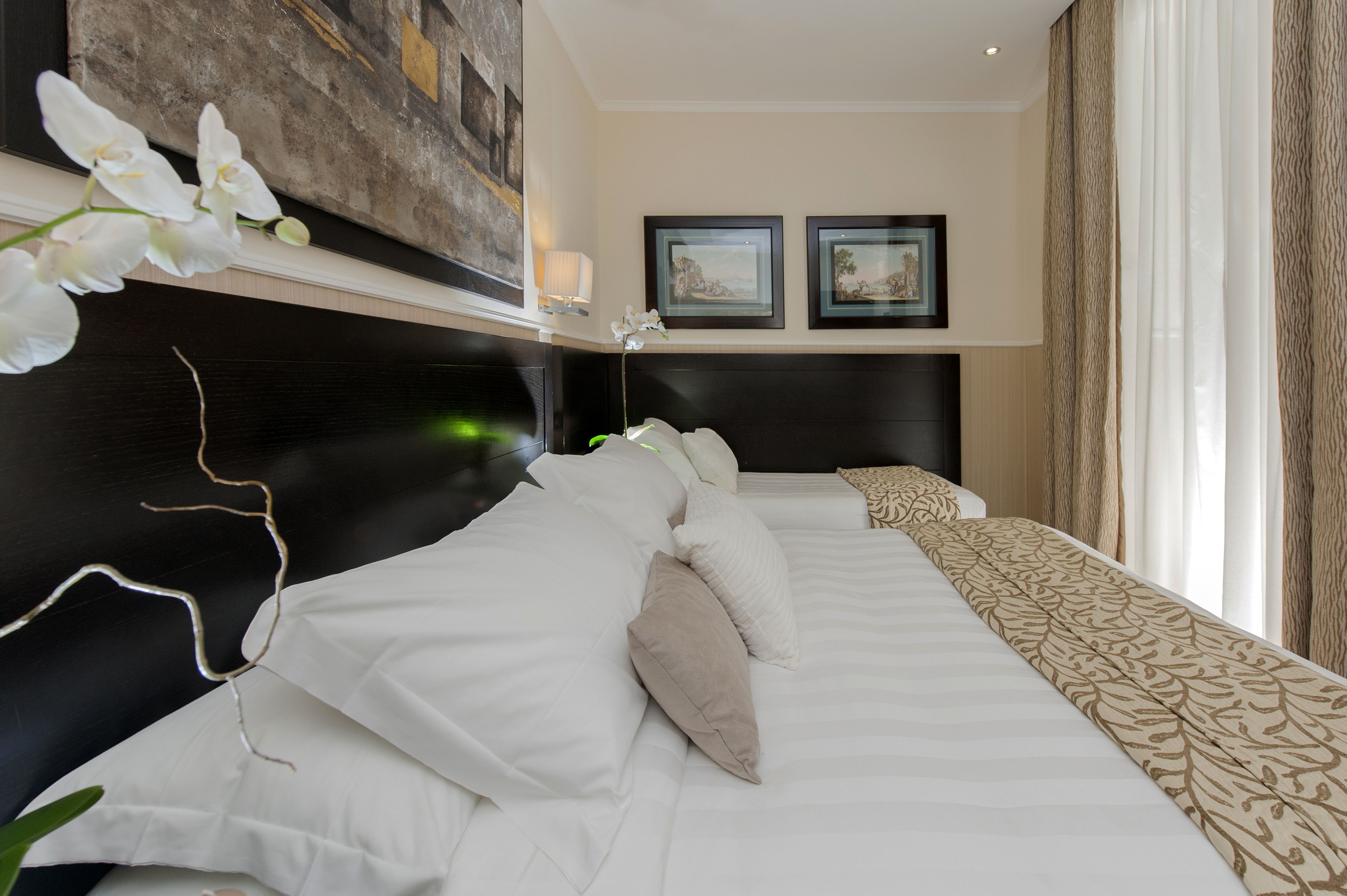 Una habitación de hotel con una cama grande, un cabecero, una obra de arte colgada en la pared y dos cuadros enmarcados.