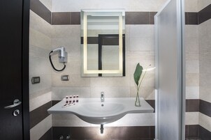 Un baño moderno con un lavamanos grande, un espejo, un perchero para toallas y un cabezal de ducha.