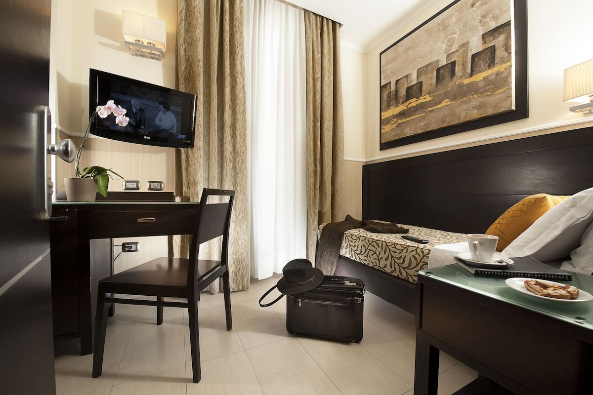 A hotel room with a desk, chair, bed, and a television mounted on the wall.