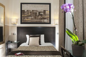 Una camera d'hotel con un letto, un comodino con una lampada, un telefono, una tazza, un libro, un quadro astratto di grandi dimensioni e un'orchidea in vaso.