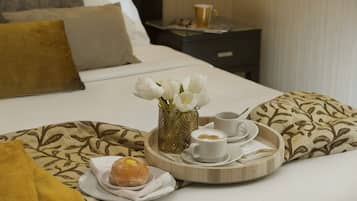 A neatly made bed with a tray of breakfast items including a donut, coffee, and a vase of flowers.