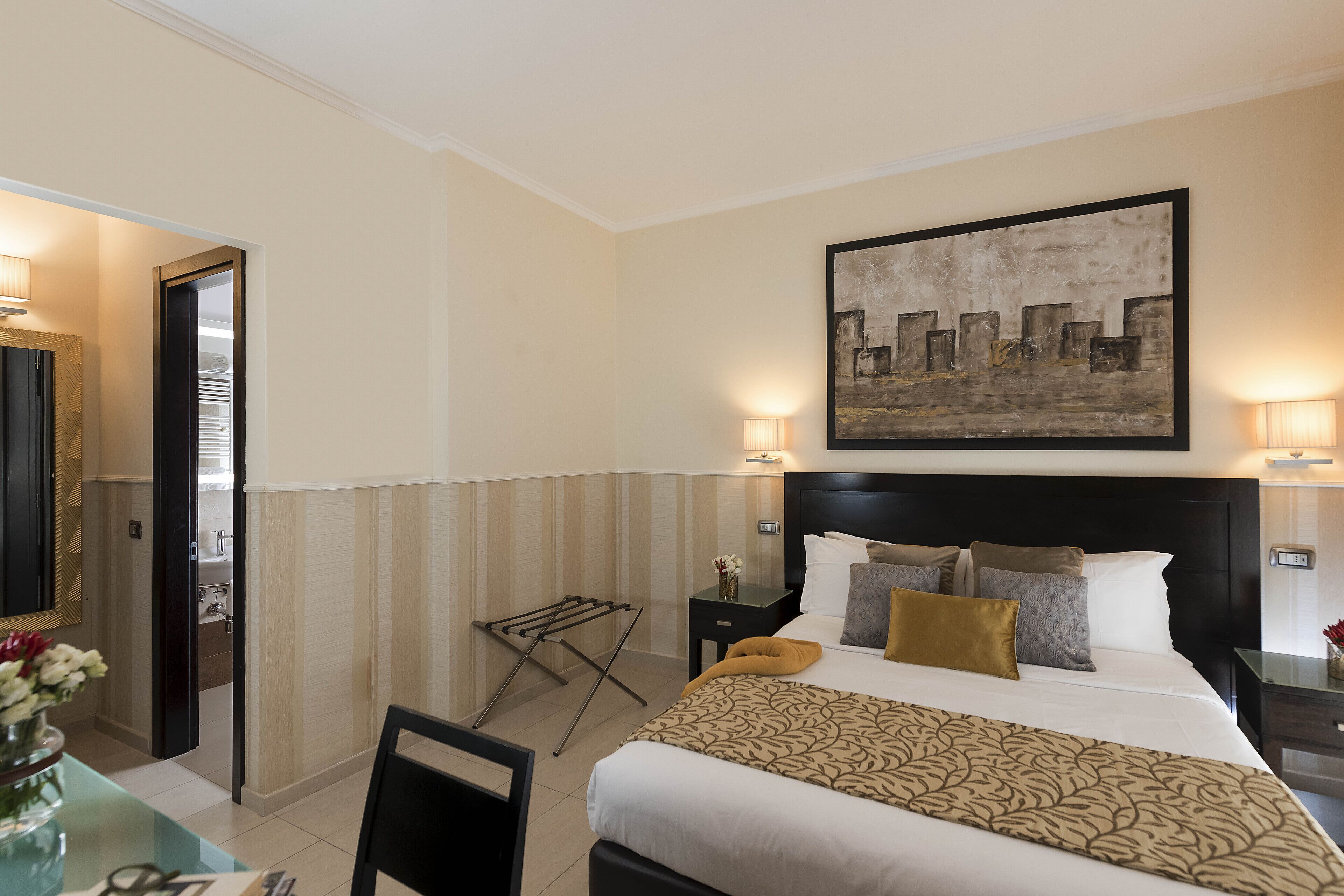 Habitación de hotel con cama, mesitas de noche, una obra de arte colgada en la pared y una zona de estar con mesa y sillas.