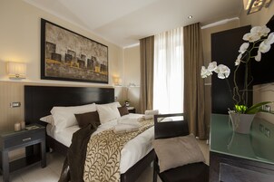 A hotel room with a large bed, a nightstand, a bedside table, a glass coffee table, a potted orchid, and a painting on the wall.