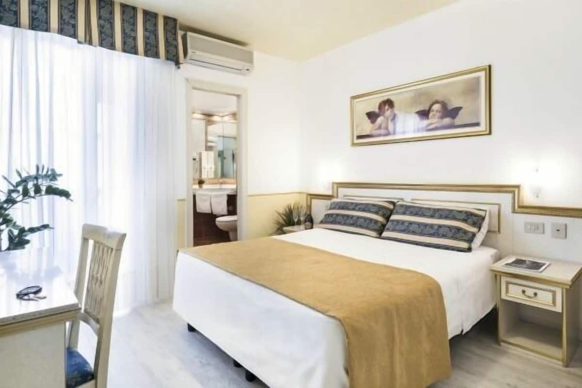 Een hotelkamer met een bed, nachtkastje en een schilderij aan de muur.