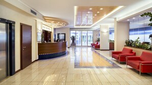 Un espace d’accueil d’hôtel avec un comptoir d’accueil incurvé, des sièges rouges et une grande plante en pot.
