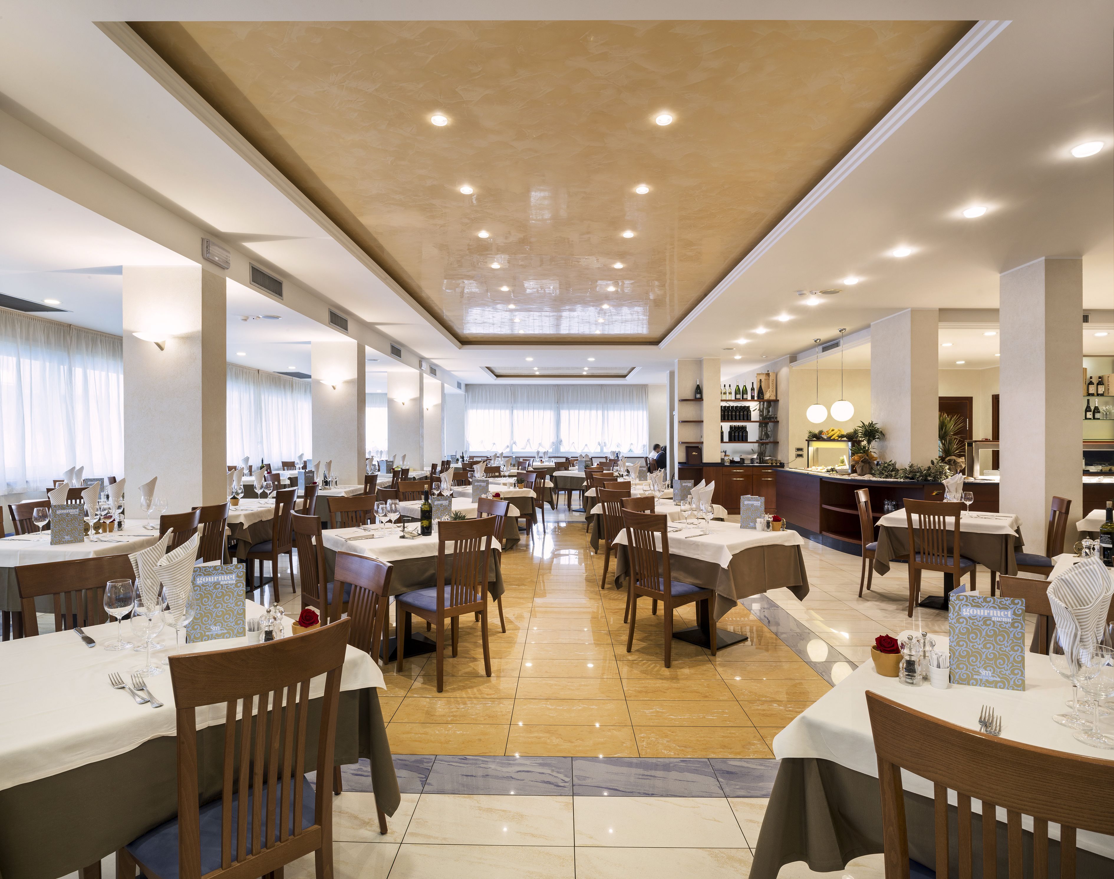 Een ruime eetruimte met meerdere tafels en stoelen, een centrale bar en een uitzicht op de eetruimte door grote ramen.