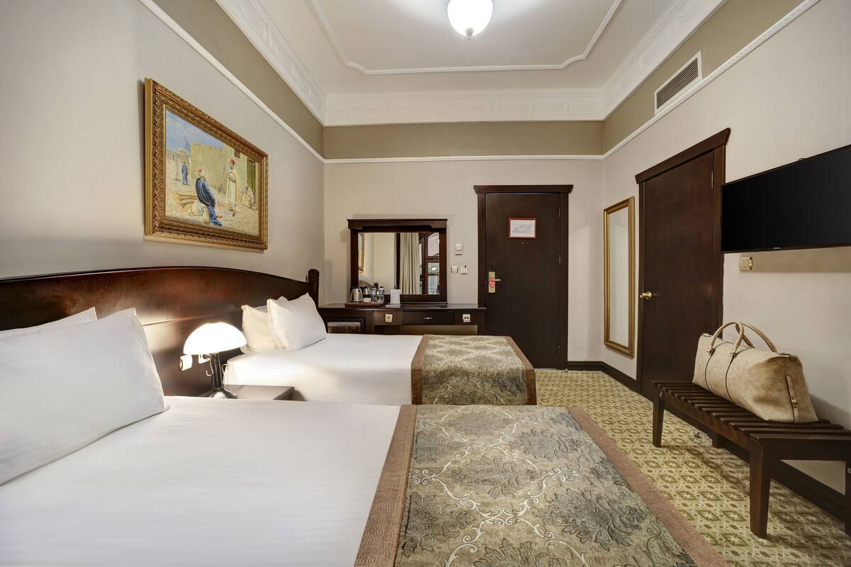 A hotel room with two beds, a sitting area, a large mirror, a wooden bench, and a painting on the wall.