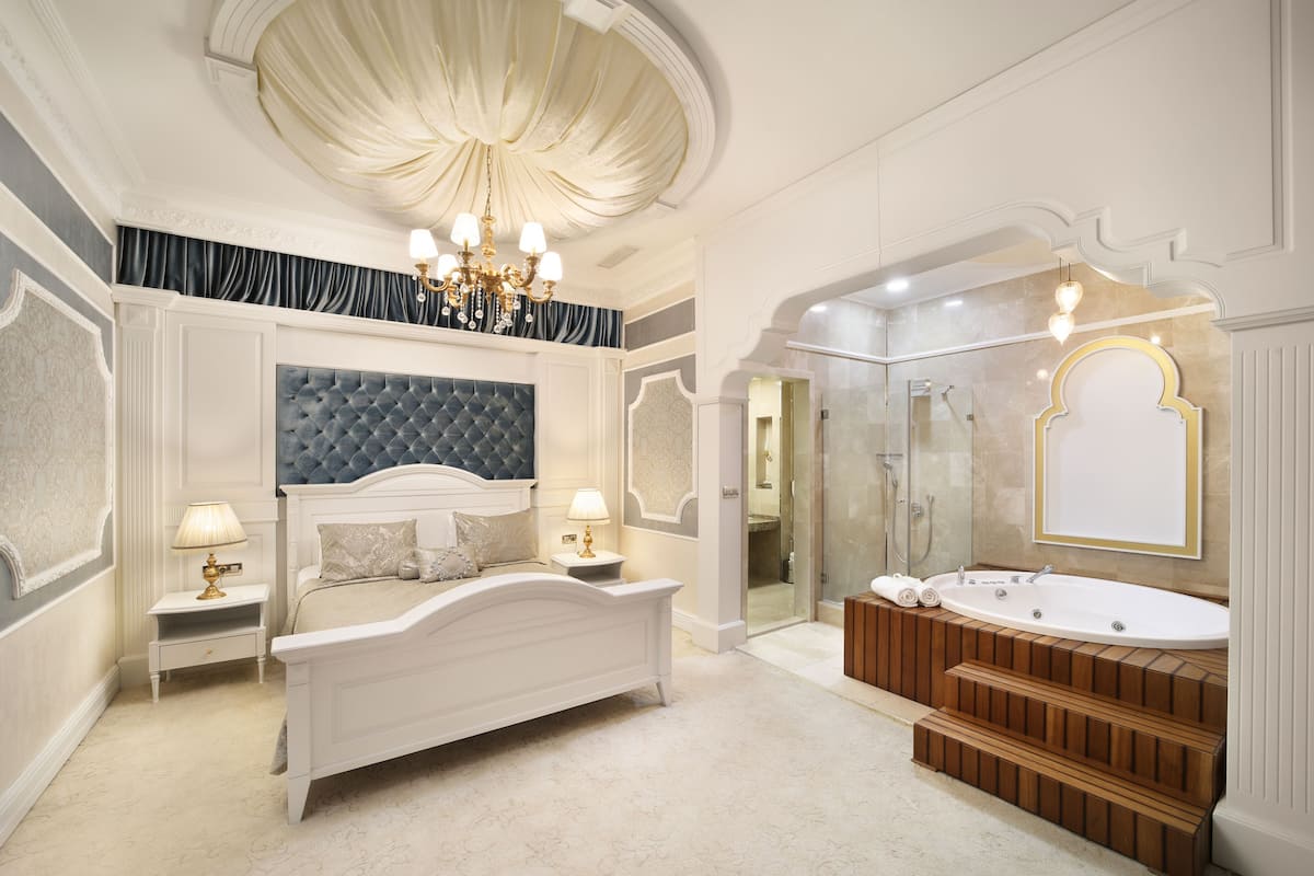 A luxurious bedroom with a large bed, a sitting area, a bathtub, and a walk-in shower.