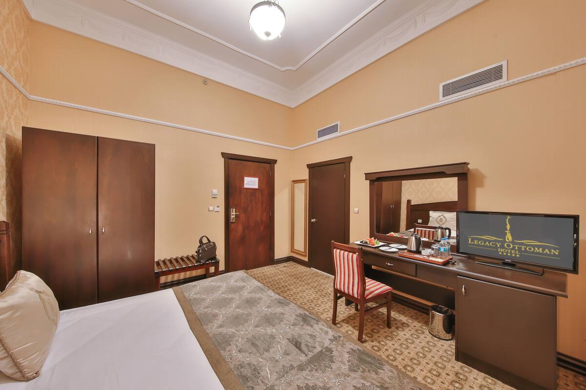 A hotel room with a bed, a desk with a television, a mirror, and a wardrobe.
