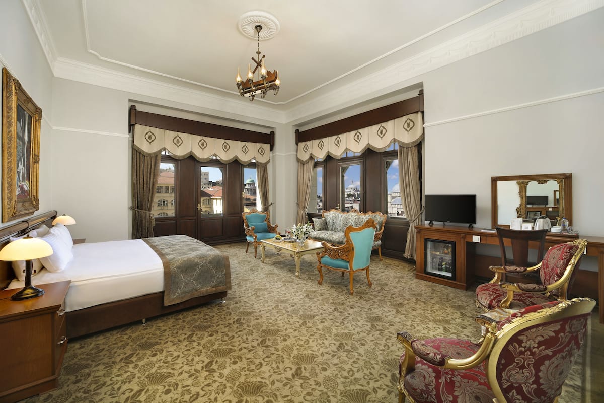 A hotel room with a bed, two armchairs, a coffee table, a TV, and a mirror.