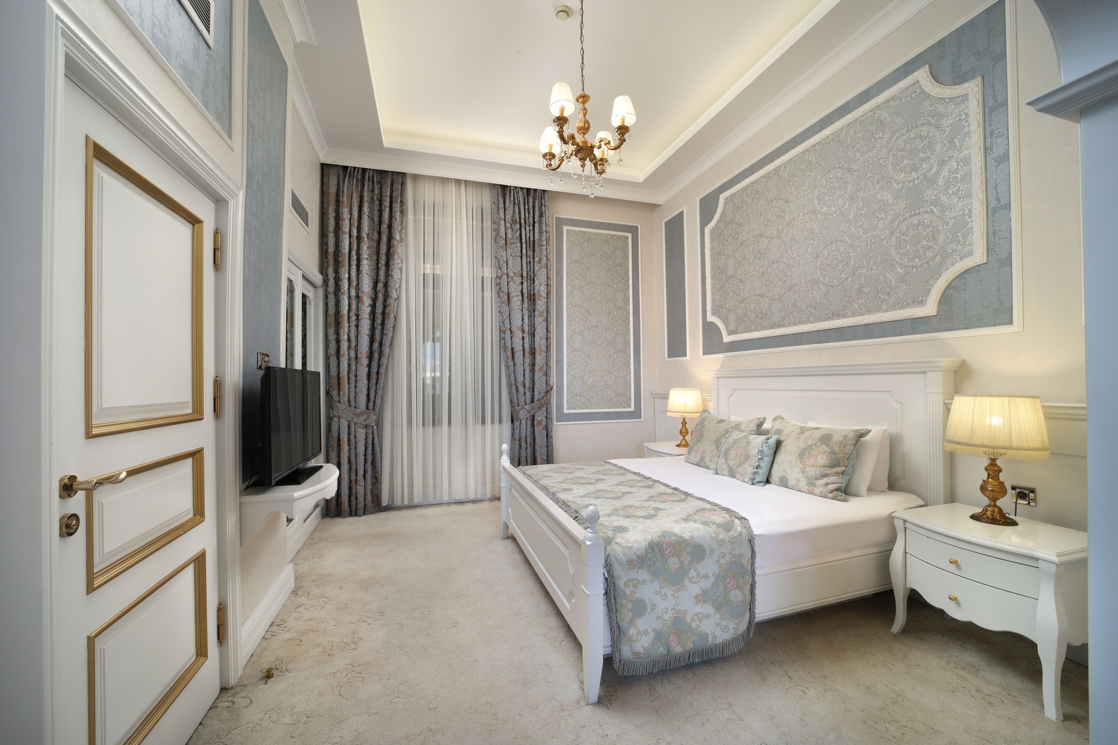 A bedroom with a bed, bedside tables, a television, and a chandelier.