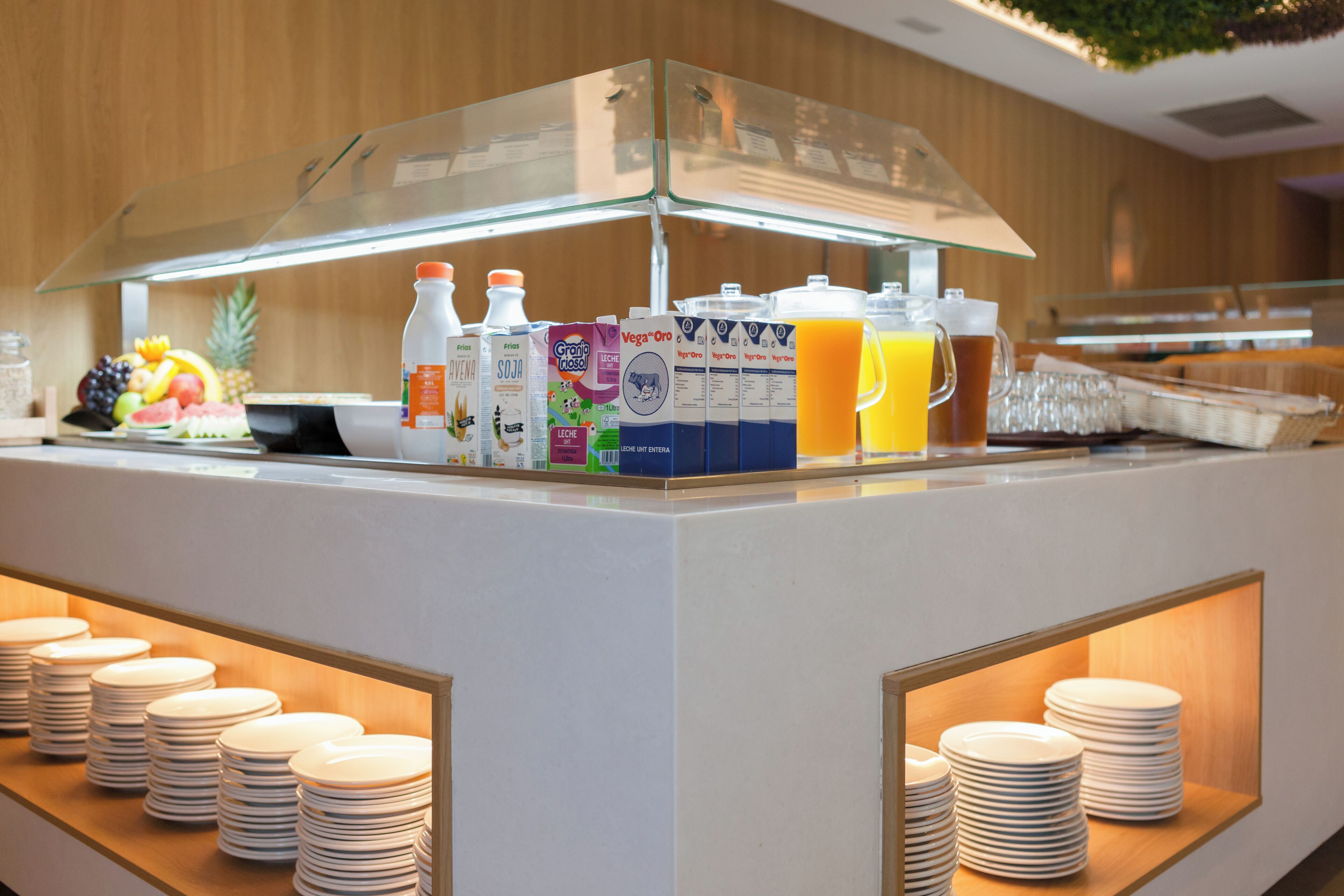 A breakfast bar with a glass display case containing various beverages and a selection of fruits.
