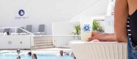 Zona de piscina con una persona sosteniendo una botella, una piscina y sillas de descanso.