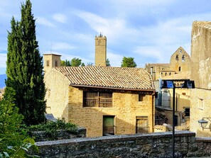 A stone building with a tiled roof, a bell tower, and a large tree in front.