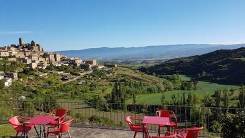 Una terraza con sillas y mesas rojas que da a un pueblo histórico con una torre destacada.