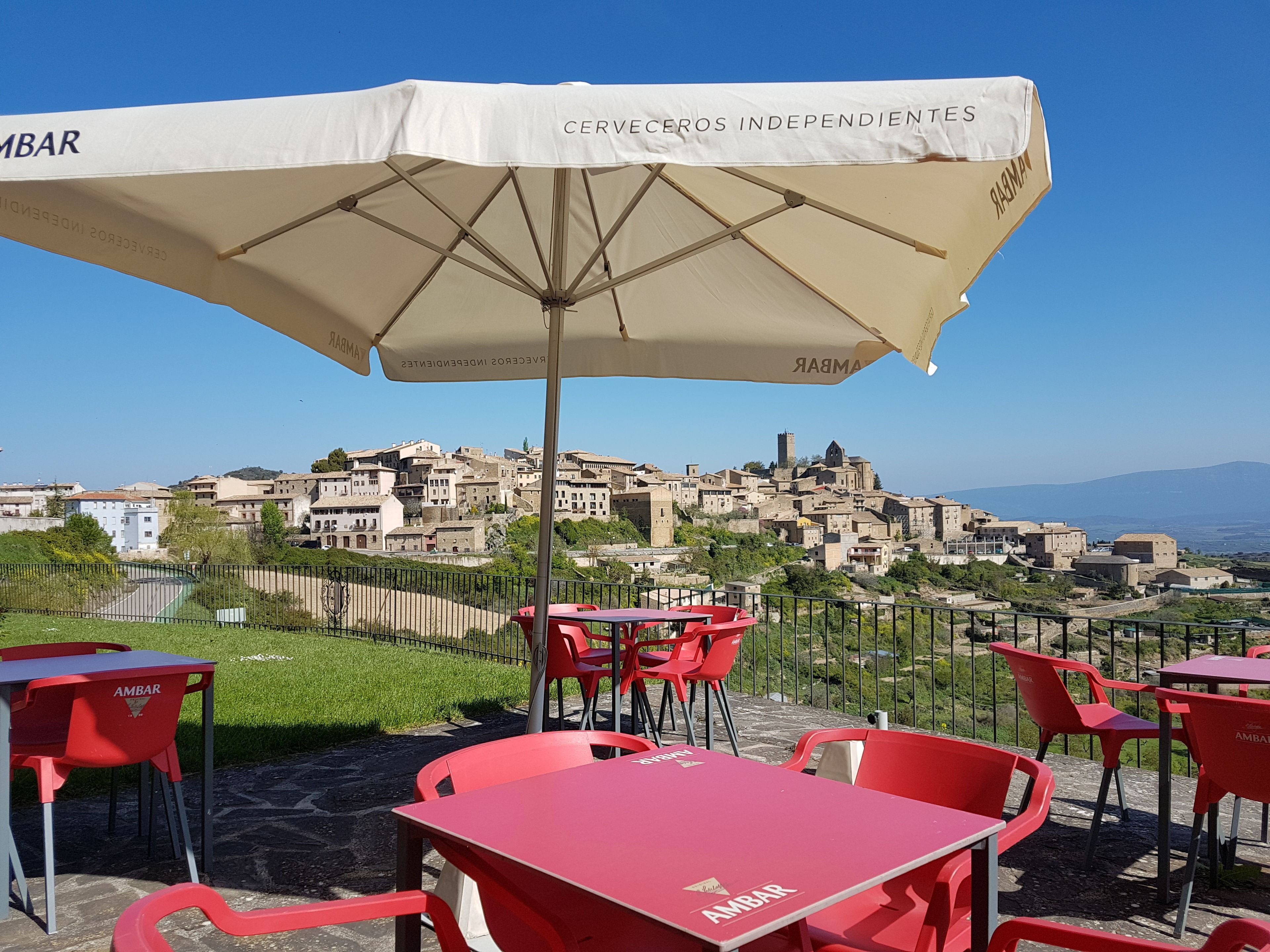 Outdoor seating with red chairs and tables, a white umbrella, and a view of a historic town in the background.