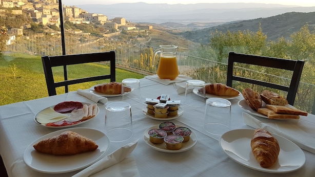 A table set with croissants, pastries, and a jug of orange juice, overlooking a mountainous landscape with a historic town in the background. - Triskel (Sos del Rey Catolico)