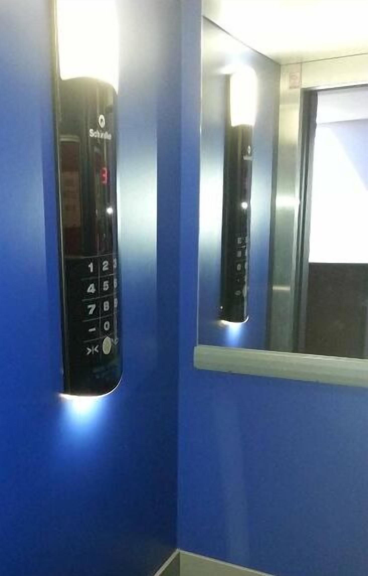 A blue elevator with a keypad and a mirror on the wall.