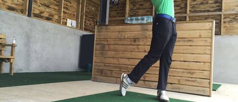 A person practicing golf swings in an indoor facility with wooden walls and artificial turf.