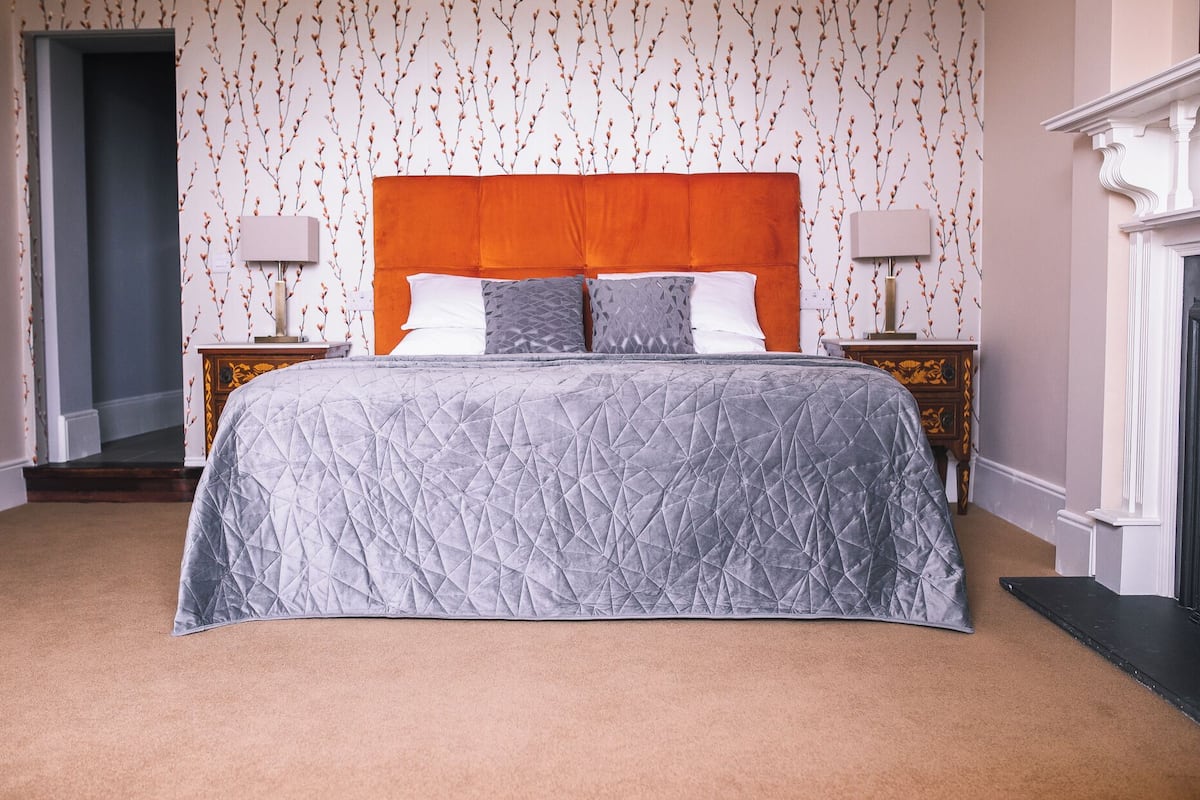 Quarto com uma cama grande, duas mesas de cabeceira, um cabeceiro de madeira e papel de parede estampado.