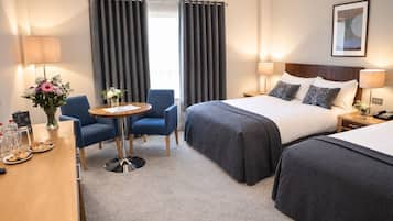 Una habitación de hotel con cama, dos sillas, una mesa con un florero y una lámpara.