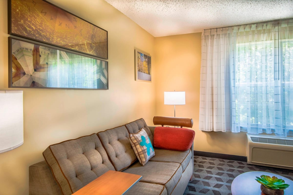 A living room with a sofa, a small table, a lamp, and a window with curtains.