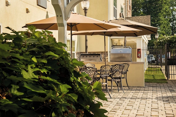 Une terrasse extérieure équipée d’un barbecue, de tables et de parasols.