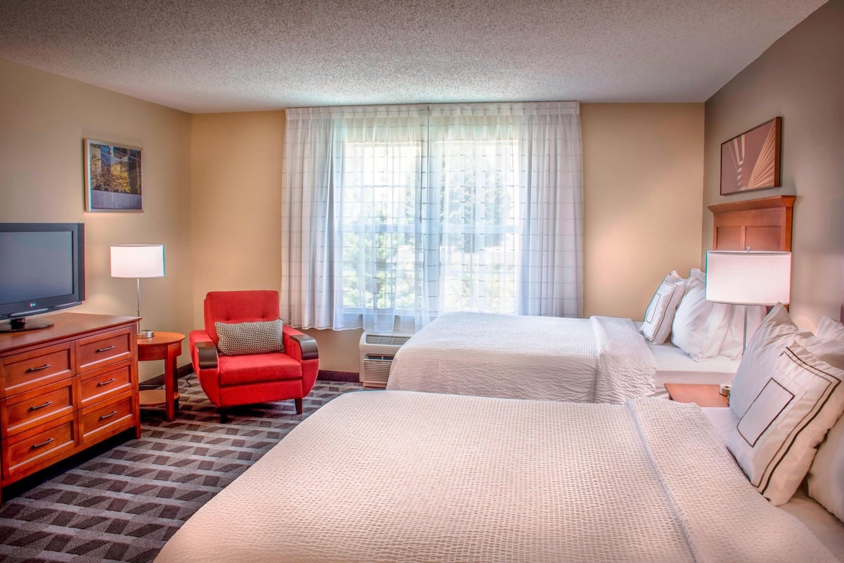 A hotel room with two beds, a red armchair, a TV, and a window with curtains.