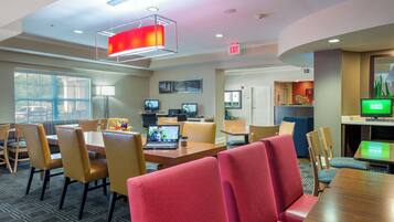 A modern hotel lobby with a dining area, multiple televisions, and a reception desk.