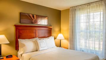 A hotel room with a wooden headboard, a bed with white bedding, two bedside lamps, a digital clock, and a window with sheer curtains.